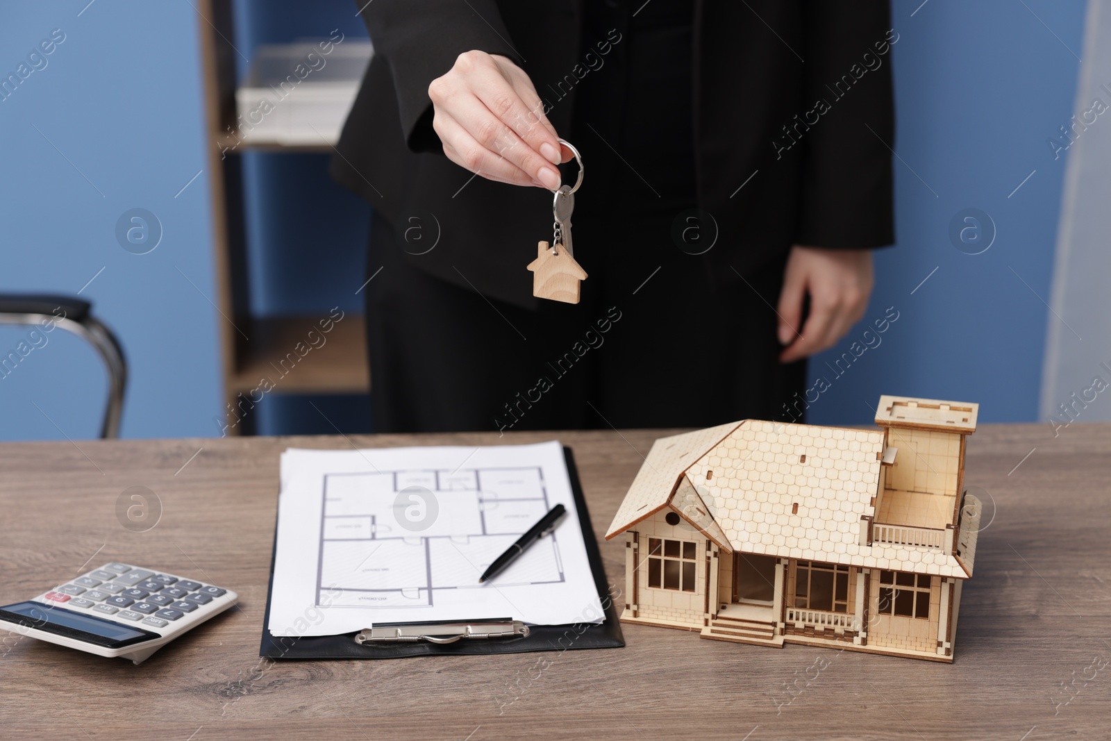 Real estate agent holding house model and key at desk in office, closeup Photo of Real estate agent holding house model and key at desk in office, closeup