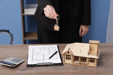 Photo of Real estate agent holding house model and key at desk in office, closeup