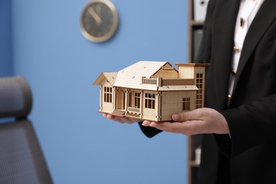 Photo of Real estate agent holding house model in office, closeup