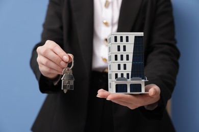 Photo of Real estate agent holding house model and key in office, closeup