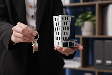 Photo of Real estate agent holding house model and key in office, closeup