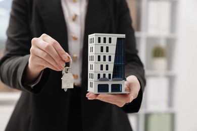 Photo of Real estate agent holding house model and key in office, closeup