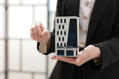 Photo of Real estate agent holding house model and key in office, closeup