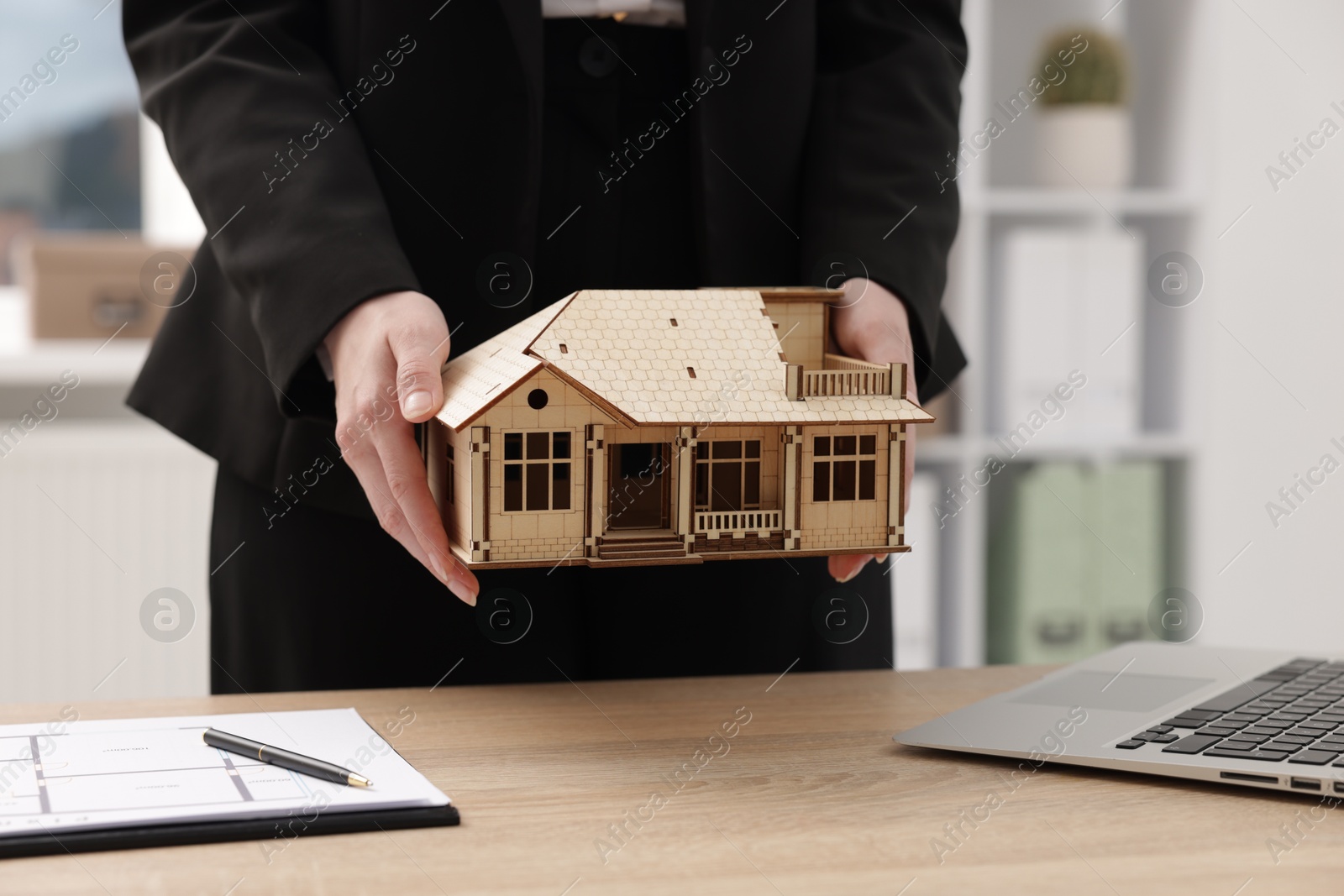 Photo of Real estate agent holding house model at desk in office, closeup