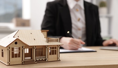 Photo of Real estate agent working at desk in office, focus on house model