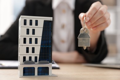 Photo of Real estate agent holding key at desk in office, focus on house model