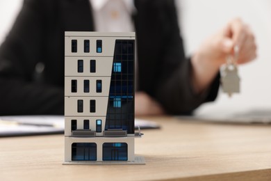 Photo of Real estate agent holding key at desk in office, focus on house model