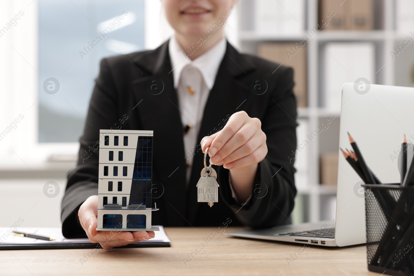 Real estate agent holding house model and key at desk in office, closeup Photo of Real estate agent holding house model and key at desk in office, closeup