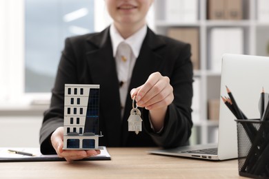 Photo of Real estate agent holding house model and key at desk in office, closeup