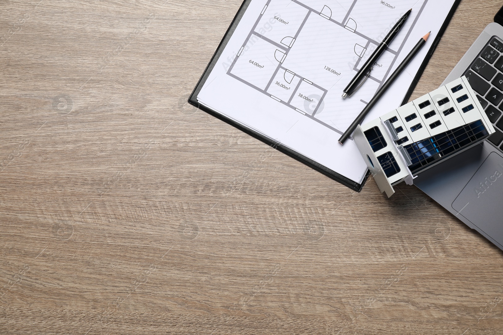 Photo of Real estate. Apartment building model, floor plan and laptop on wooden table, flat lay. Space for text