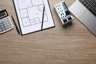 Photo of Real estate. Apartment building model, floor plan, calculator and laptop on wooden table, flat lay. Space for text