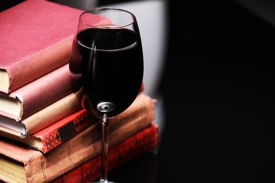 Photo of Red wine in glass and stack of books on dark background, closeup. Space for text