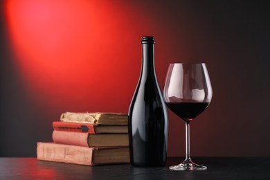 Photo of Tasty wine and stacked books on dark table in red light, closeup