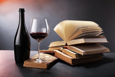 Photo of Tasty wine and books on dark textured table in color light, closeup
