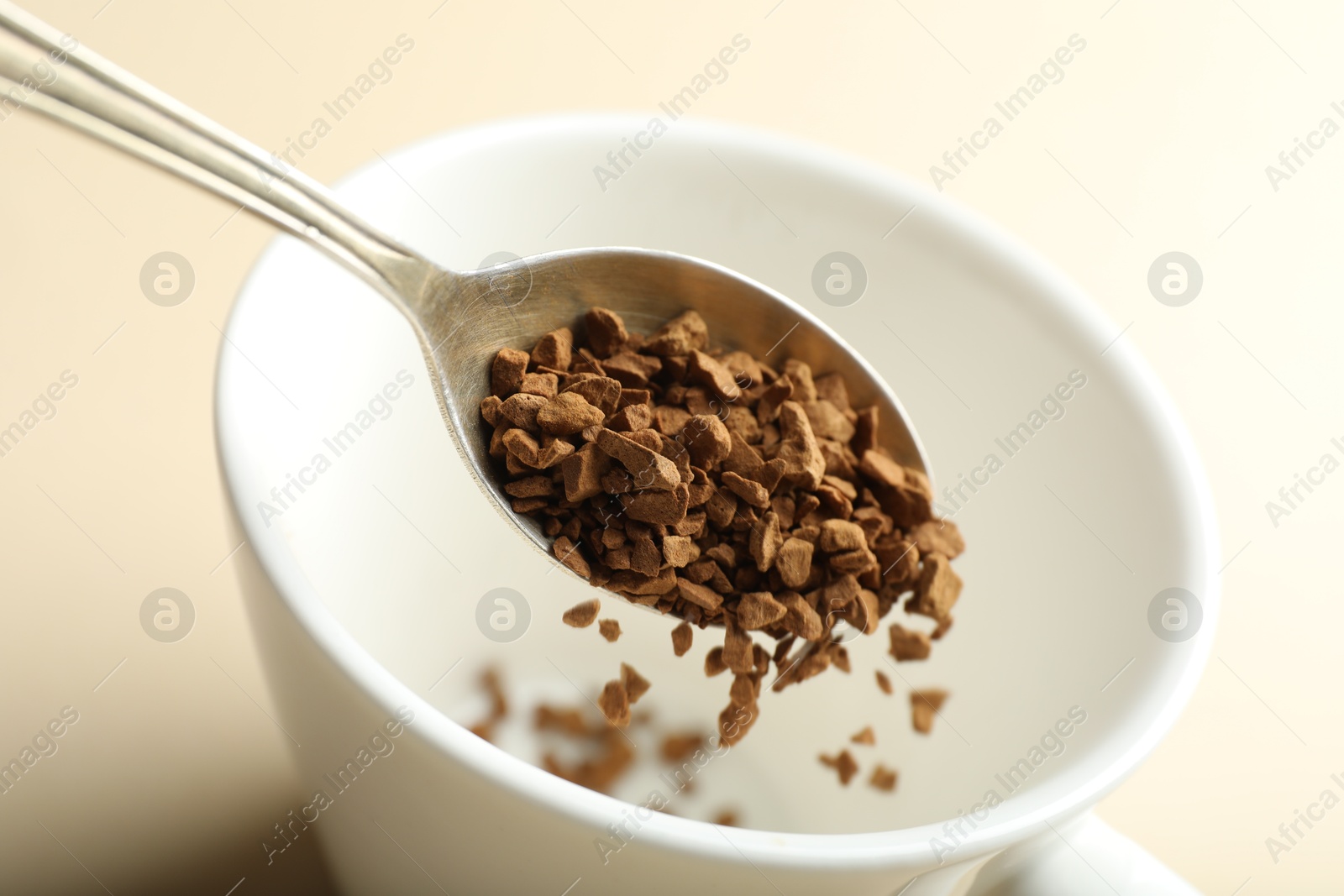 Photo of Putting instant coffee into cup on beige background, closeup