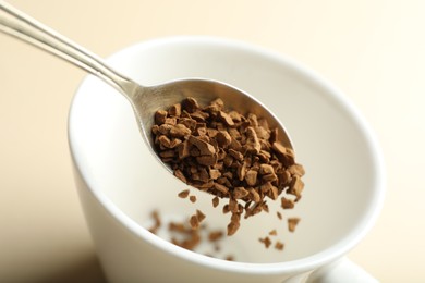 Photo of Putting instant coffee into cup on beige background, closeup