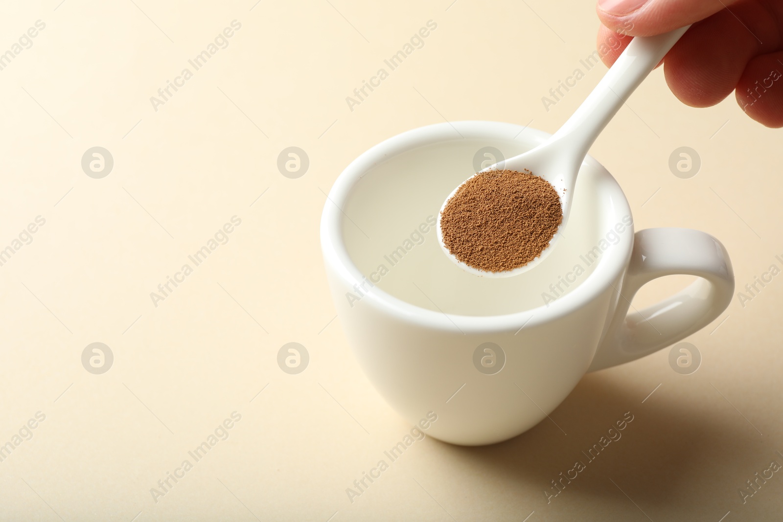 Woman putting instant coffee into cup on beige background, closeup. Space for text Photo of Woman putting instant coffee into cup on beige background, closeup. Space for text