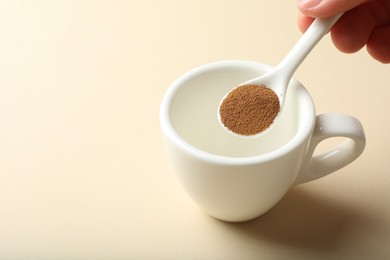 Photo of Woman putting instant coffee into cup on beige background, closeup. Space for text