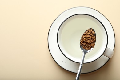 Photo of Spoon with instant coffee above cup on beige background, top view. Space for text
