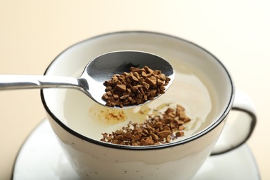 Photo of Putting instant coffee into cup on beige background, closeup