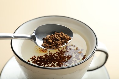 Photo of Putting instant coffee into cup on beige background, closeup
