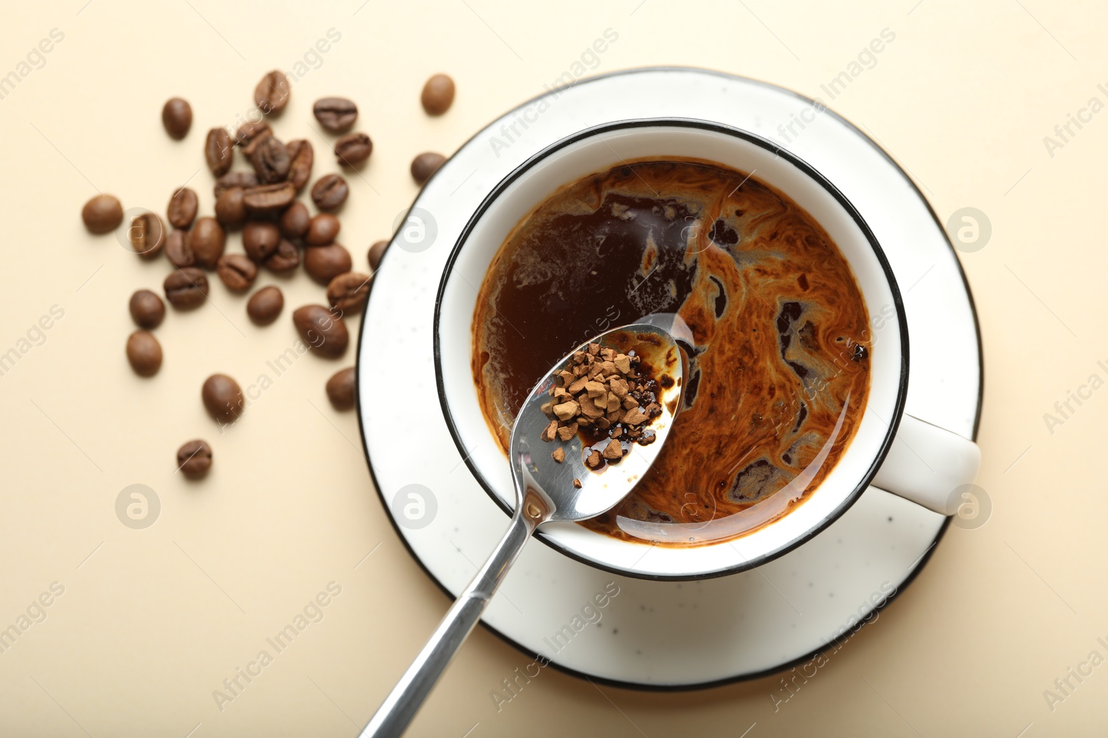 Putting instant coffee into cup on beige background, top view Photo of Putting instant coffee into cup on beige background, top view
