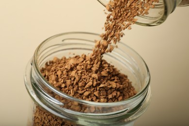 Photo of Pouring instant coffee into jar on beige background, closeup