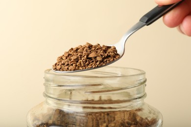 Photo of Woman taking instant coffee with spoon on beige background, closeup