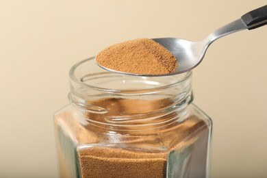 Photo of Taking instant coffee with spoon on beige background, closeup