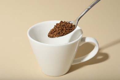 Photo of Putting instant coffee into cup on beige background, closeup