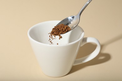 Photo of Putting instant coffee into cup on beige background, closeup