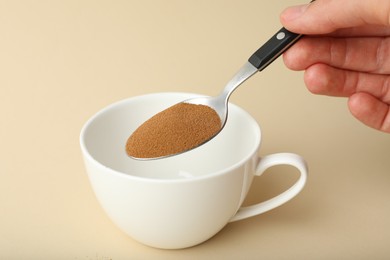 Photo of Woman putting instant coffee into cup on beige background, closeup
