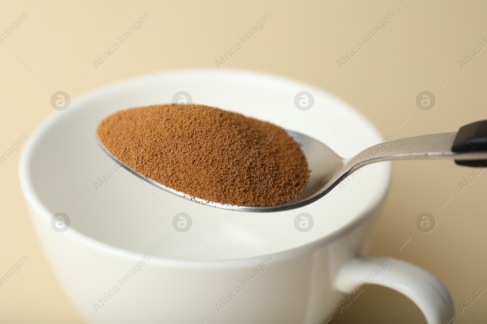 Spoon with instant coffee and cup on beige background, closeup Photo of Spoon with instant coffee and cup on beige background, closeup