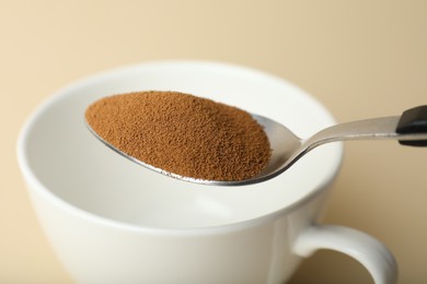 Photo of Spoon with instant coffee and cup on beige background, closeup