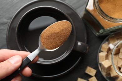 Photo of Woman holding spoon with instant coffee above cup at black table, top view