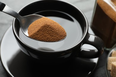 Photo of Putting instant coffee into cup at table, closeup