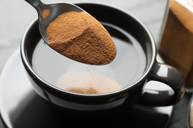Photo of Putting instant coffee into cup at table, closeup