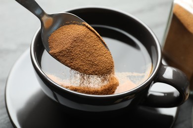 Photo of Putting instant coffee into cup at table, closeup