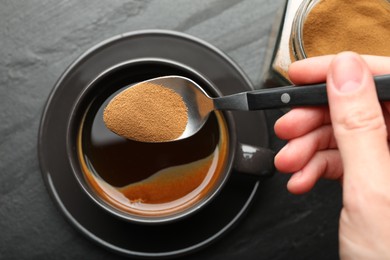 Photo of Woman putting instant coffee into cup at black table, top view