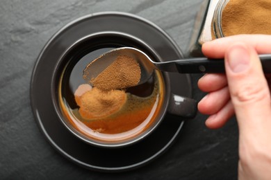 Photo of Woman putting instant coffee into cup at black table, top view