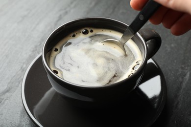 Photo of Woman stirring instant coffee with spoon at black table, closeup