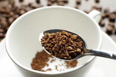 Photo of Spoon with instant coffee and cup on table, closeup
