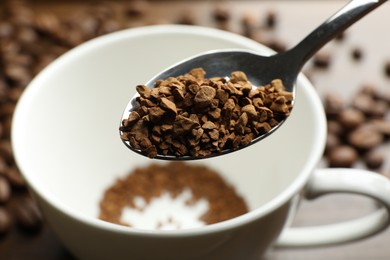 Photo of Spoon with instant coffee and cup on table, closeup