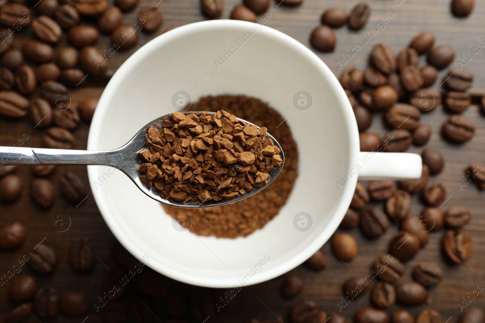 Photo of Spoon with instant coffee above cup and beans on wooden table, top view