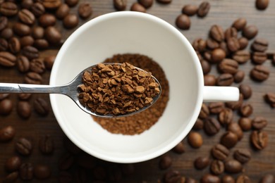 Photo of Spoon with instant coffee above cup and beans on wooden table, top view