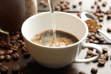 Photo of Pouring hot water into cup with instant coffee at wooden table, closeup