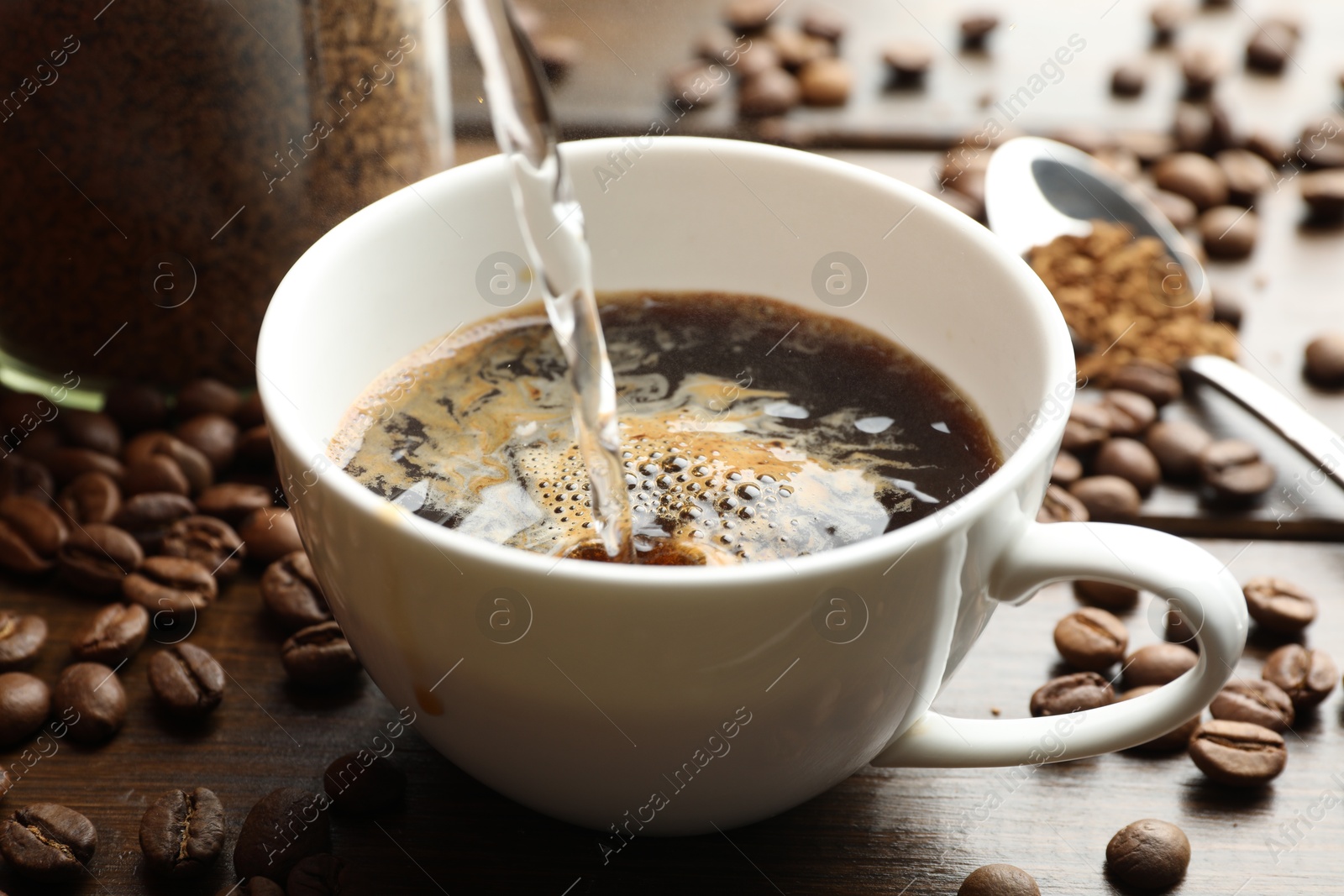 Pouring hot water into cup with instant coffee at wooden table, closeup Photo of Pouring hot water into cup with instant coffee at wooden table, closeup