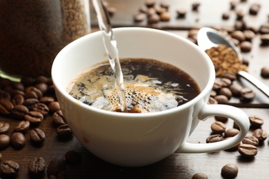 Photo of Pouring hot water into cup with instant coffee at wooden table, closeup
