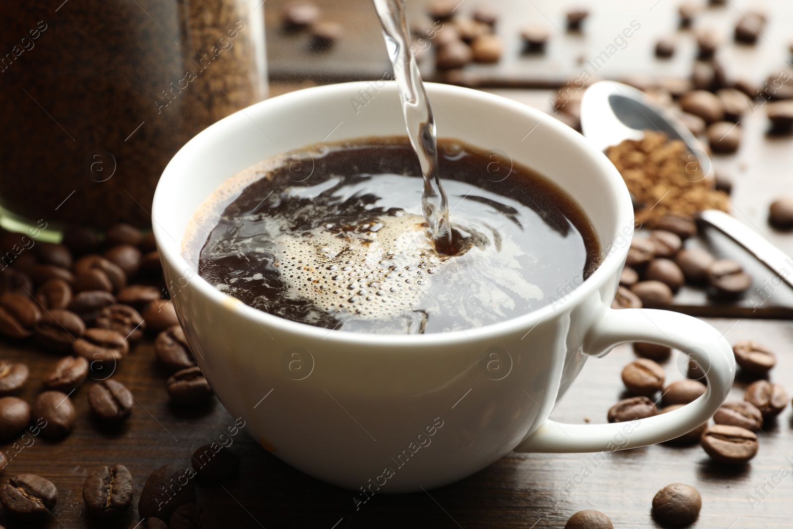 Photo of Pouring hot water into cup with instant coffee at wooden table, closeup