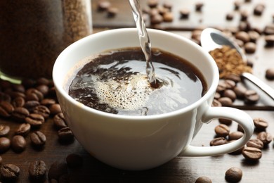 Photo of Pouring hot water into cup with instant coffee at wooden table, closeup